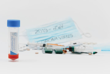 a test tube with a positive test for the CAVID-2019 coronavirus. medical devices on a white table. thermometer, phonendoscope, tablets, surgical masks