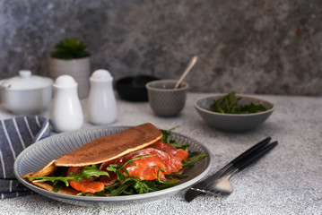 Crepe with arugula and salmon for breakfast on the kitchen table. Good morning.