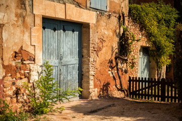 Fototapeta na wymiar Old house with big light blue gate in one of the most beautiful villages of France Roussillion, Provence. Stone walls painted in ohra color. Travel tourism destination Provence in hot sunny day
