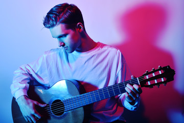 Obraz premium A man plays an acoustic guitar in neon red-blue light. A man learns to play the guitar, music, hobbies.