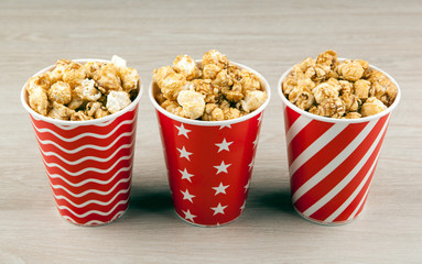 three red cardboard cup in a row with sugar popcorn on a wooden table