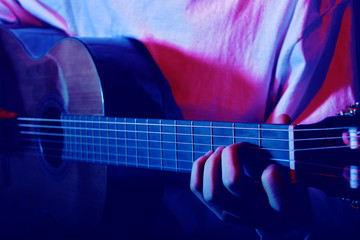 Close-up of fingers on the neck of an acoustic guitar. Muchina plays the guitar in neon. Musician, music, training.