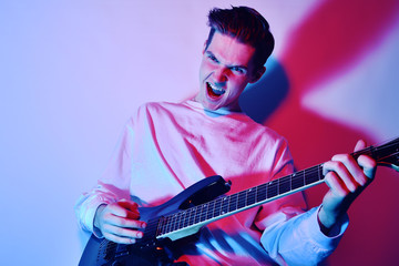 Obraz premium A man plays the electric guitar in neon light, red blue light. Hobbies, music, club. A man enjoys playing the guitar, screaming, vivid emotions.