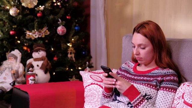 Portrait of a lonely sad woman sitting near the christmas tree with mobil phone. concept of holidays and new year.