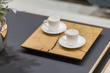 Modern wooden stand and two white coffee cups on a coffee table. Beautiful dishes on the table in detail