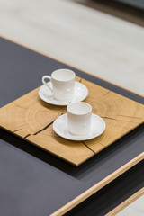 Modern wooden stand and two white coffee cups on a coffee table. Beautiful dishes on the table in detail