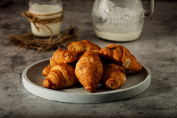 Freshly baked French croissants with cappuccino milk on a dark background with copy space.