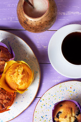 Top view on sweet muffins cupcakes and cup of coffee on purple desk