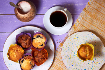 Top view on sweet muffins cupcakes and cup of coffee on purple desk