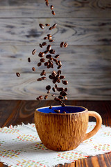 Big cup on a wooden table with coffee beans falling inside