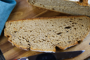 Close up of fresh made german stoneoven bread, cut slice and brown white loaf with crunchy crust on wooden cutting board
