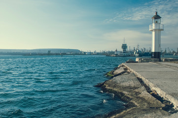 Fototapeta premium lighthouse in coast city port with blue sky and water, beacon for ship and yacht navigation