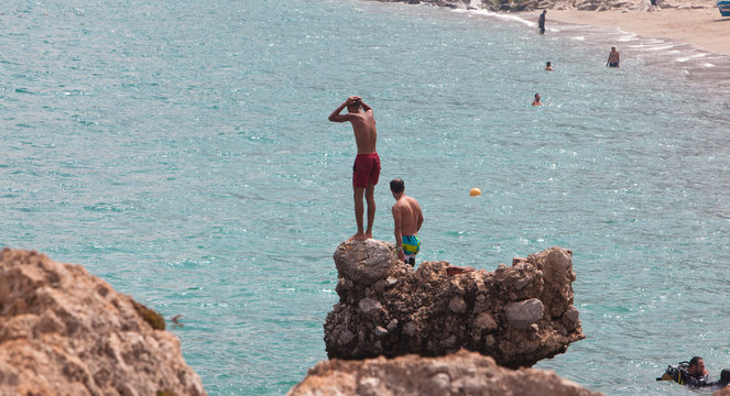 belyounech, Morrocco - 25 june 2017: Young man jumping off cliff into blue water ocean at sunset. holiday adventure on the Moroccan beach,