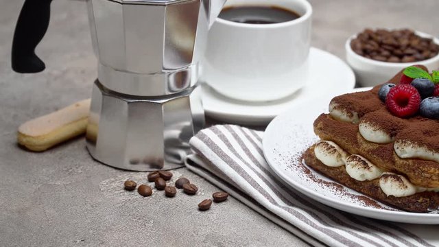 portion of Classic tiramisu dessert with berries, espresso, coffee maker on grey concrete background