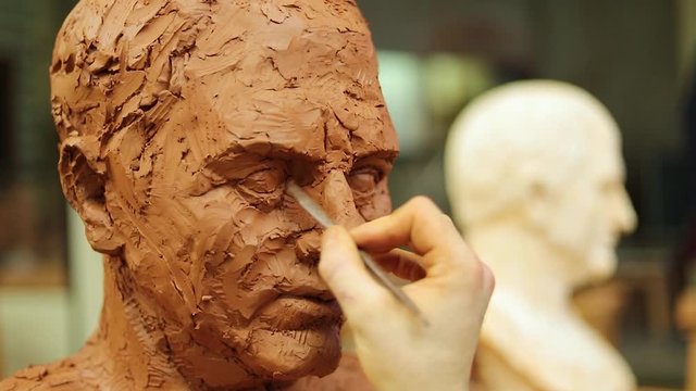 Hand of sculptor finishing a clay head eye in an art studio