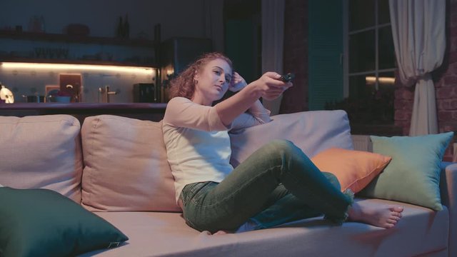 Young woman switching TV channels with remote control relaxing in evening