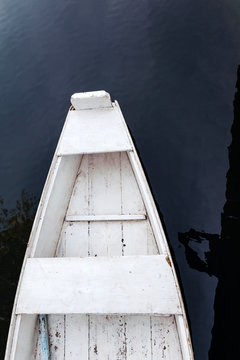 The bow of an old white rowing boat, shot from above on a background of water.