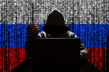 Russian hacker in the hood threatens with his fist against the backdrop of a tricolor from a binary...