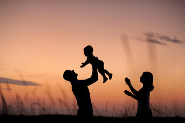 Silhouettes of family on the background of the evening sky. Parents play with the child in nature.