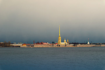 Fototapeta na wymiar Saint-Petersburg, Russia. River and buildings illuminated by the sun against a dark clouds. Famous tourist landmark - Peter and Paul Fortress. 