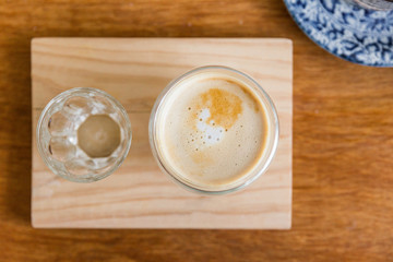 Top view of hot latte in a glass cup with a glass of water on wooden plate. 