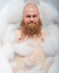 Portrait of a bald man fooling around in the foam bath. Top view on guy having fun in the bathroom.