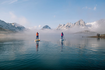 Two women stand up paddle surfing on a lake
