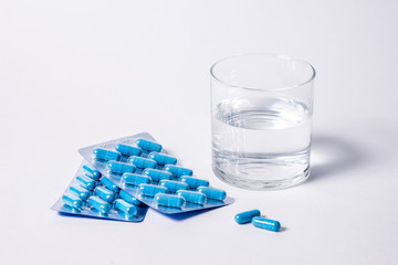 Two packages of blue capsules and a glass water. Pills for men's health and sexual energy. Concept of erection, potency. Treatment of male infertility and impotence and prostatitis