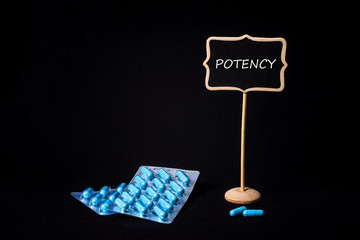 Two packs of blue capsules and the word potency on a chalkboard. Pills for men's health and sexual...