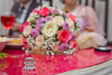 Obraz na płótnie Canvas Bride and groom with Engagement gold rings put on the table, and next to them lies a wedding bouquet .red table . Wedding rings next to a flower bouquet selective focuse . Colorfull Wedding flowers .