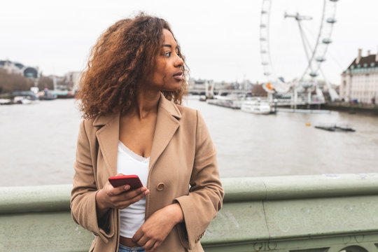 Young woman with cell phone in the city and Lonon Eye in background, London, UK