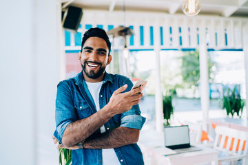 Naklejka premium Cheerful guy surfing phone in summer cafe