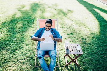 Expressive guy working with notepad and laptop in park