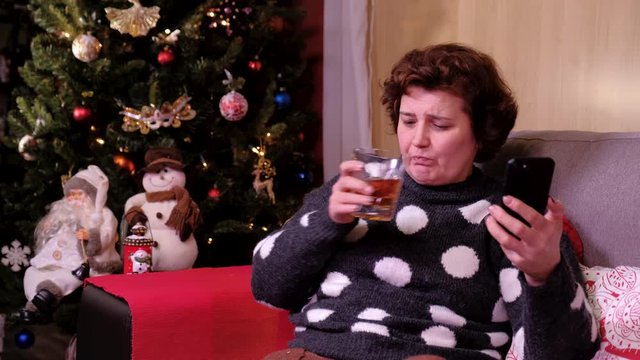 Portrait of a lonely sad woman sitting near the christmas tree with mobil phone. concept of holidays and new year.