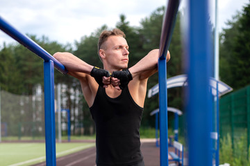 Obraz premium A muscular man stands leaning on parallel bars, with a bare torso.