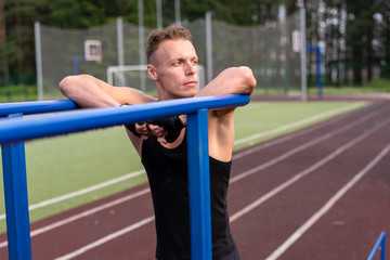 A muscular man stands leaning on parallel bars, with a bare torso.