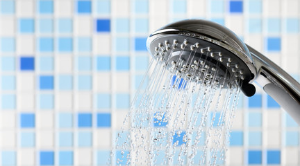 Shower head with flowing water stream in blue bathroom - obrazy, fototapety, plakaty