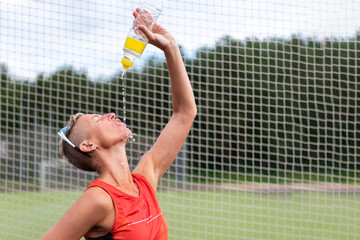 A sports woman drinks water and poured water on her.