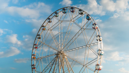 White clouds and rotating ferris wheel at festival or carnival. Summer cloudy day, warm illumination, sunset blue sky. Sightseeing, cityscape, entertainment, holiday, leisure time concept