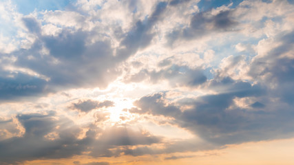 Sun beams shining through dramatic white clouds. Cloudy blue sky, warm sunrise or sunset...