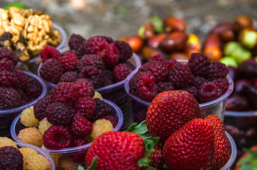 Ripe fruits in glasses for street sale. Red and white raspberries, strawberries figs, nuts. Travel and adventure.