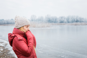 Young woman standing by the frozen lake in winter morning