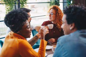 Four friends talking in a cafe, enjoying themselves while drinking coffee.