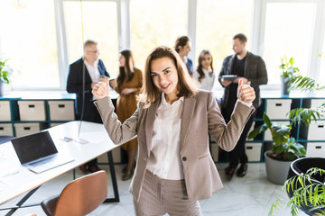 Young happy businesswoman with win gesture standing in front of her team.