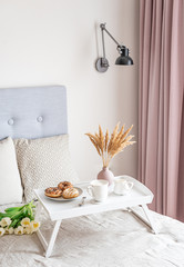 Breakfast in bed, cup with cappuccino, doughnuts, flowers white tulips, morning concept, linen bed sheets, woman's day