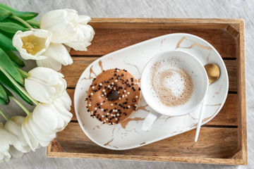 Breakfast in bed, cup with cappuccino, doughnuts, flowers white tulips, morning concept, linen bed sheets, woman's day