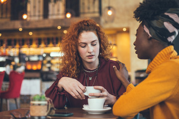 A young woman is talking with a female friend about her problem in a cafe. The friend is supportive...