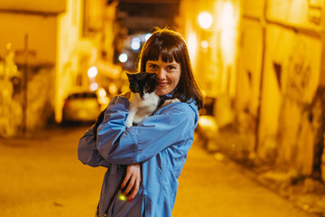 Cat. Girl stroking a cat against the backdrop of the night city. Italy.