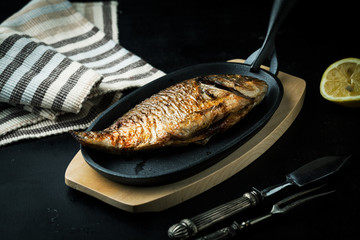 Fried fish in a frying pan on a dark