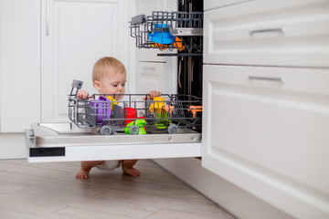 baby loads the dishwasher with plates and his toys. little helper